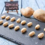 Gnocchi di patate freschi su un piano di lavoro con ingredienti pronti per la preparazione.