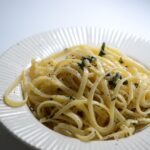 Pasta al limone con crema vellutata e scorza di limone grattugiata, servita in un piatto bianco.