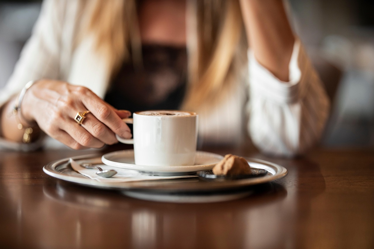 Tazza di caffè fumante su un tavolo, con piatto vuoto e posate, simbolo di un rituale post-pranzo.