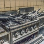 Friggitrice ad aria abbandonata su un bancone, circondata da cibo non utilizzato e segni di polvere.